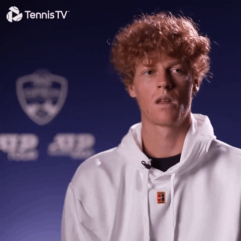Video gif. Interview with tennis player Jannik Sinner stretching out his mouth wide in a big yawn, looking bored or uninterested. Logo appears at the top corner for "TennisTV."