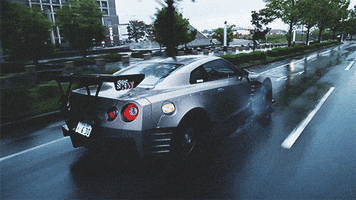 Video gif. Silver Nissan GT-R sports car speeding down a wet street.