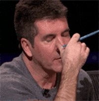 Reality TV gif. Simon Cowell holds a pen between his fingers as he rubs his eyes irritably.