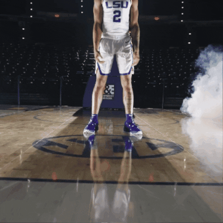 Sports gif. LSU basketball player wearing a jersey with the number two on it spreads his arms wide with his head tilted back in celebration as he stands in front of a glowing basketball hoop.