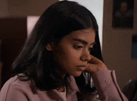 Movie gif. Radhika Apte in "It Lives Inside" turns to look over her shoulder with a questioning expression, holding one hand behind her ear in a timid or uncomfortable way. 