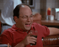 Seinfeld gif. Jason Alexander as George winks and points his finger across the table.