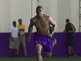 Sports gif. Football star Adrian Peterson sprints topless in slow motion, showing off his jacked arms and impressive 8-pack.