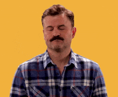 Video gif. Mustachioed man closes his eyes and shakes his head in disappointment, scrunching his chin and pursing his lips.