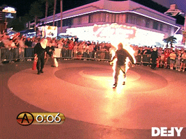 TV gif. From Criss Angel Mindfreak, a man whose body is engulfed in flames walks forward easily through a gated empty space, around which a crowd watches.
