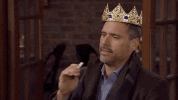 TV gif. Joshua Morrow as Nicholas in The Young and The Restless. He has a crown on and dejectedly blows a party horn, staring off into space as he does so, clearly unexcited for his birthday. 