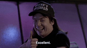 Movie gif. Mike Myers as Wayne in Wayne's World smiles as he looks at us and nods his head, giving a thumbs up. Text, "Excellent."