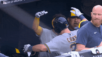 Sports gif. Willy Adames and Mark Canha on the Brewers hug tightly as they jump up and down in the dugout; one is wearing a batter's helmet like he's just scored a run. 