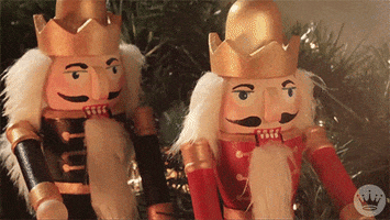 Stop motion gif. Two wooden nutcrackers, one in a red coat and the other in a blue coat, drop their jaws and arms as if shocked at something. Walnut chunks fall out of the mouth of the nutcracker in blue.