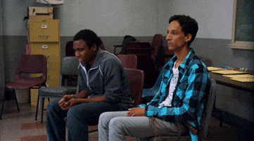 TV gif. Donald Glover as Troy and Danny Pudi as Abed from Community are sitting together waiting nervously. We zoom in on Troy as he begins to rock back and forth intensely, holding his breath and pursing his lips together.