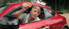 Video gif. Man in a polo and a tied sweater sits in a red car, telling someone to come on and hurry up. He rudely hits the side of the car to get their attention and snaps his fingers in the air.