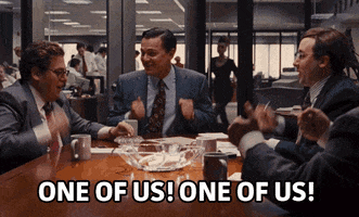 Movie gif. Leonardo Dicaprio as Jordan, Jonah Hill as Donnie, and several other characters in Wolf of Wall Street sit around a meeting table, banging their fists in unison onto the table. They excitedly cheer together, “One of us! One of us!”