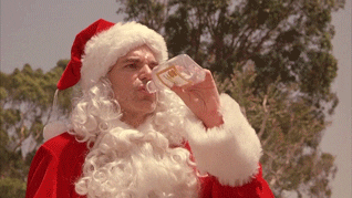 Movie gif. Billy Bob Thornton as Willie Soke in Bad Santa wears his Santa costume but has the white beard pulled down so that he can easily chug a bottle of alcohol while he lumbers around outside.