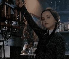 Movie gif. Christina Ricci as as Wednesday Addams from the Addams Family pulls an old electrical lever that sparks as it’s pulled down. She has a bored expression on her face and barely even flinches when the lever sparks near her face.