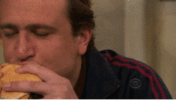 TV gif. Jason Segel as Marshall in How I Met Your Mother rolls his eyes in sheer bliss as he takes a bite from a hamburger. 