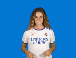 Video gif. Woman wearing a Real Madrid jersey that says "Emirates Fly Better" gives us two thumbs up and a big smile against a bright blue background.