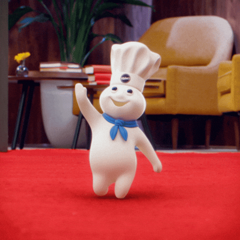 Sponsored gif. The Pillsbury Doughboy, in his iconic blue scarf and Pillsbury chef hat, walks a red carpet and waves as if greeting an audience. 