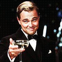 Leonardo DiCaprio ve filmu Velký Gatsby, zvedající číši se šampaňským na pozadí vybuchujících ohňostrojů v gifu.