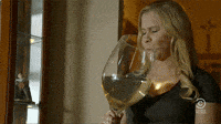 Celebrity gif. Amy Schumer holding a ginormous glass of wine that's bigger than her head. She closes her eyes and holds the glass in two hands as she begins to chug the wine. She drinks sloppily, letting the wine run down her face and shirt, as she drinks in rapture.