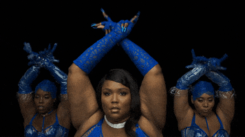Celebrity gif. Lizzo is performing at the Savage x Fenty show and she's dancing with her arms up in the air. She's wearing lacy gloves and does a hand dance as the dancers in the back perform in unison.