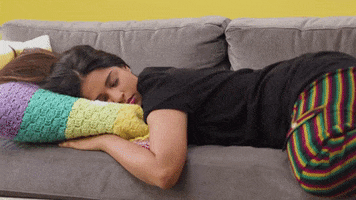 Celebrity gif. Lilly Singh is passed out on a couch, sleeping face down. She gets woken abruptly, looking as if she's heard or smelled something strange, and she glances around in confusion. 