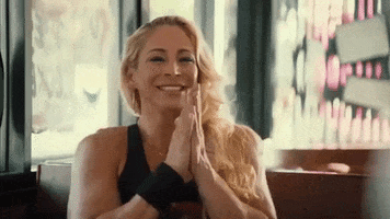 Video gif. Buff woman claps eagerly, smiling while sitting in a booth.