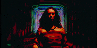 Music video gif. Briston Maroney cast in red lighting standing in front of a trippy infinite hallway.
