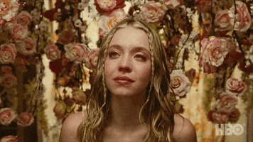 TV gif. Sydney Sweeney as Cassie on Euphoria surrounded by bundles of roses with tears streaming down her face.
