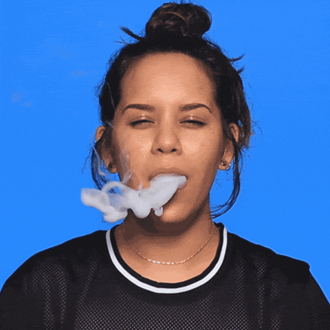 Digital art gif. Young woman with a messy bun and squinty eyes blows smoke at us, fully obscuring our view, and the smoke dissipates into the words "Shabbat Shalom."
