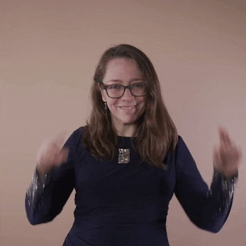 Reaction gif. A Disabled Latina woman with brown wavy hair and glasses excitedly snaps with both hands.