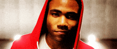 Music video gif. From the video for Freaks and Geeks, Childish Gambino half-smiles, looking up at us, wearing a red hoodie.