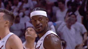 Video gif. Slow motion clip of Miami Heat player Jimmy Butler looking back over his shoulder and winking at someone in a playfully taunting sort of way.