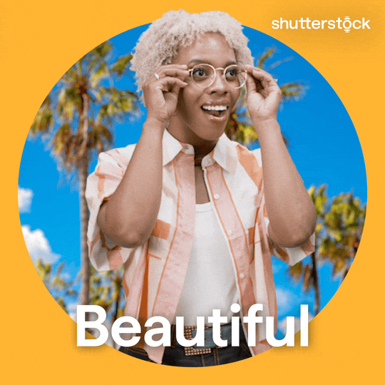 Sponsored gif. Woman takes off her glasses and looks around with a wide-eye expression of wonder on her face. The background behind her features palm trees on a sunny day. Text reads, “Beautiful.”