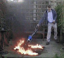 Video gif. A man calmly pushes a vacuum back and forth over burning turf. The vacuum glides over the flames until they are all extinguished. Then the man strikes a proud pose near the burnt patch. 