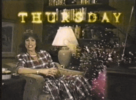 Video gif. A woman in the 80s is sitting in her living room as fireworks go off in the background. She looks at them in surprise and the text reads, "Thursday."