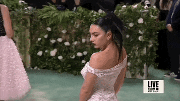 Met Gala 2024 gif. Closeup of Charli XCX showing the back of her white Marni gown with hand-sewed rhinestones and glass beads made of ripped patchworked well-worn t-shirts with holes throughout. The top of the off-the-shoulder dress resembles a ripped and worn t-shirt neckline with large holes  stretching straight across her upper back.