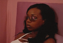 Celebrity gif. We see Tiffany Pollard in a closeup looking bored or angry. We back up to see she sits in bed dressed to go out with boots and sunglasses on, her hands folded in her lap. 