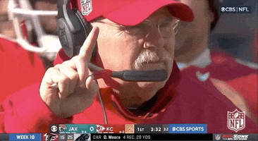 Sports gif. Andy Reid, head coach of the Kansas City Chiefs, stands on the sidelines during a game. He holds up one finger in the air. 