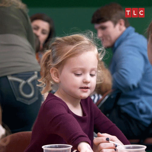 a little girl is sitting at a table with two cups of water .