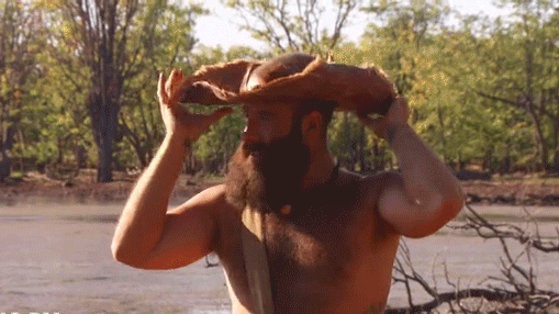 Gif of a topless white man with a wild beard standing on a beach, putting on a decrepit straw hat and smiling. Captions says: STYLE