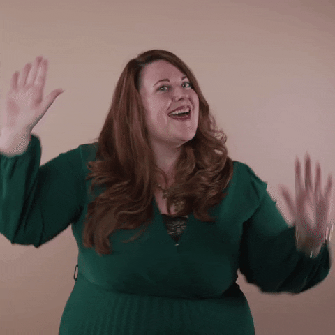 Reaction gif. A non-apparently Disabled white woman with with anxiety and depression and long red hair waves her arms and shakes her hips, doing a happy dance.