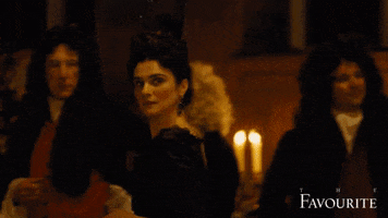 Movie gif. With a fixed gaze, Rachel Weisz as Sarah Churchill in "The Favourite" steps in front of partygoers, pivots to turn and points to someone.