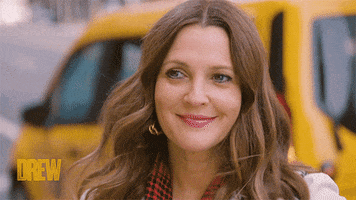TV gif. Closeup of Drew Barrymore standing in front of a taxi as she smiles and winks flirtatiously on her eponymous show.