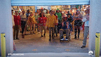 TV gif. At the Superstore holiday party, the costumed workers gather around the bay door as the snow falls magically.