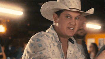 Music video gif. In the video for Fill 'Er Up, Jon Pardi raises his beer and smiles, sitting at a bar with friends.