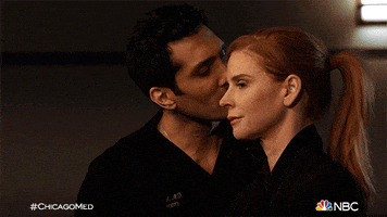 TV gif. Dominic Rains as Crockett on Chicago Med rubs the shoulder of Sarah Rafferty as Pamela and kisses her on the cheek, while she smiles mildly.