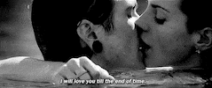 Music video gif. From the "Blue Jeans" video, Lana Del Rey wraps her arms around a man, neck deep in a body of water, french kissing.