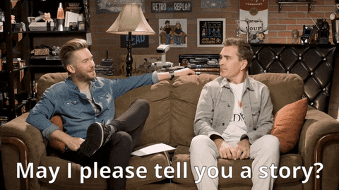Gif of two white men sitting on a sofa (Troy Baker and Nolan North). One says "may I please tell you a story?" and the other replies "please tell me a story", smiles and crosses his legs to get into an active listening pose