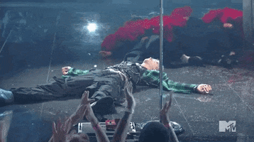 Celebrity gif. Machine Gun Kelly lays flat on the stage breathing heavily after his performance at the 2021 VMAs. The camera pans around him and we see his chest moving up and down quickly.