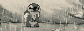 Disney gif. Black-and-white scene of Stitch from Lilo and Stitch standing in the rain and crying pitifully.